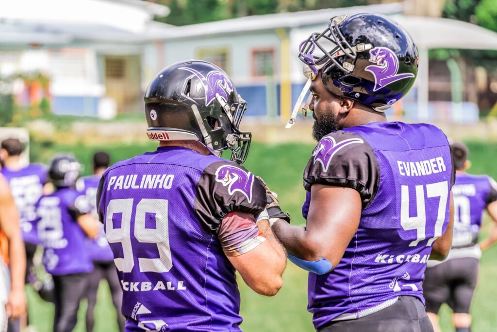 Two American football players in purple jerseys and helmets preparing on the field.